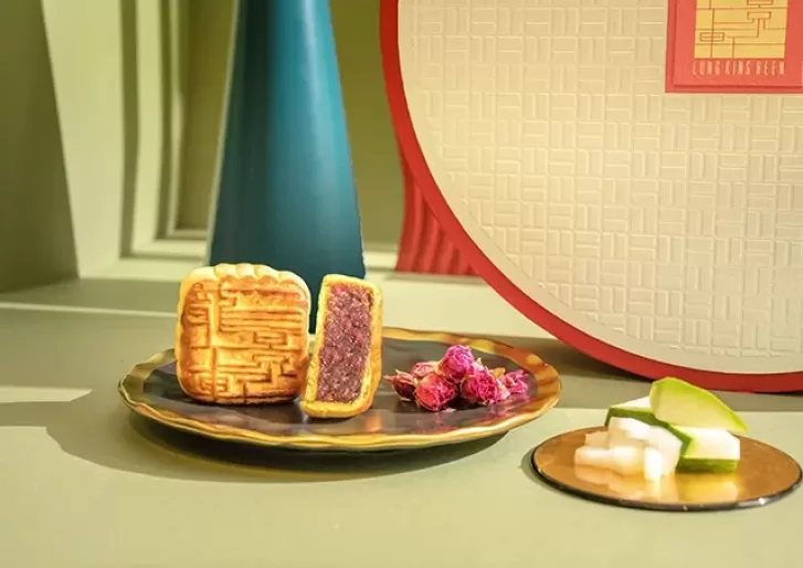 A plate holds two winter melon mooncakes next to an assortment box and a plate of garnises, showcasing a charming dessert arrangement.