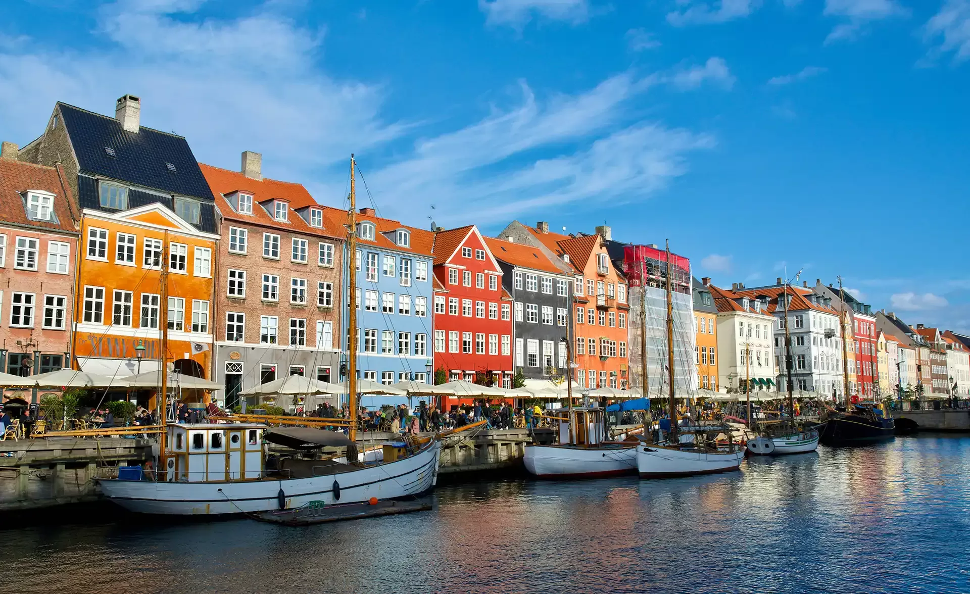 Colorful historic buildings and moored boats line the Nyhavn waterfront canal in Copenhagen, Denmark, under a clear blue sky.