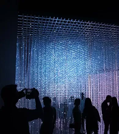 Black silhouettes of people walking through and taking pictures of a light exhibition in a gallery