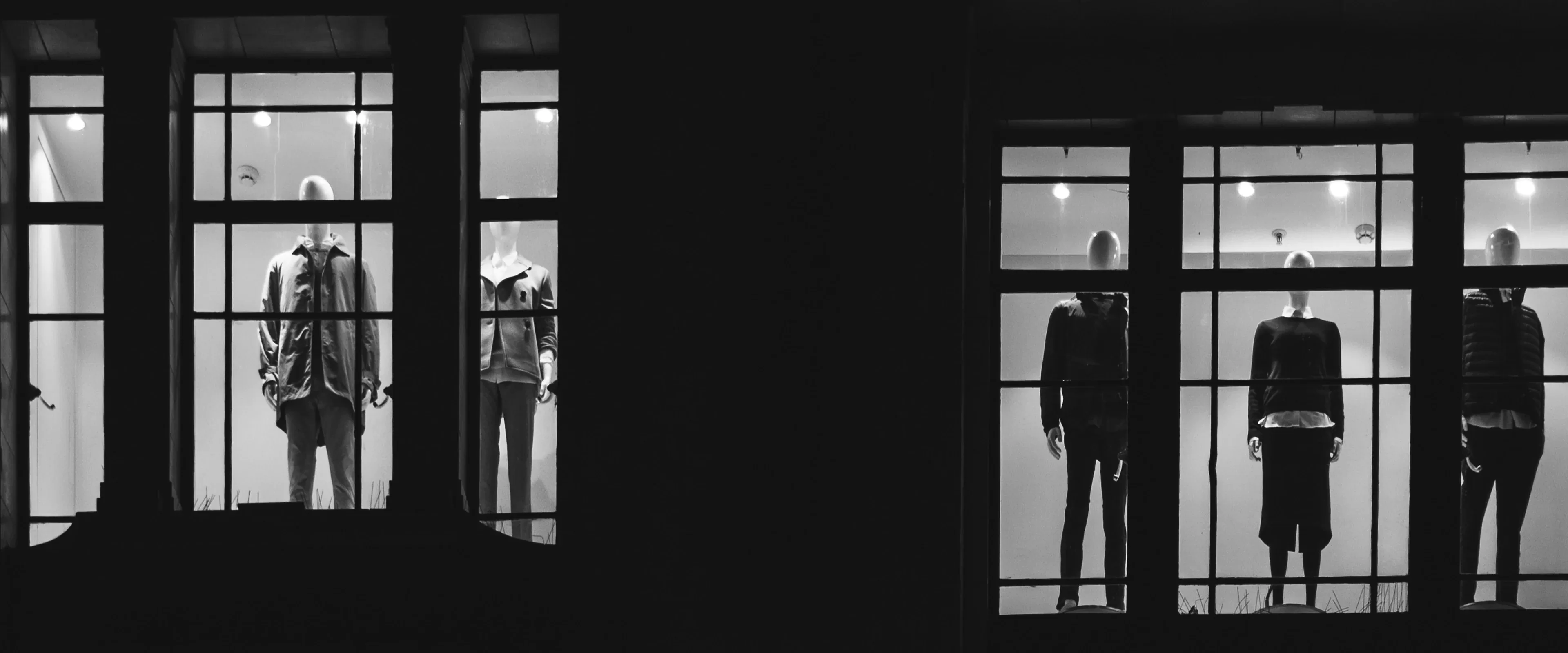 Black and white photo of window display of mannequins wearing men and women's fashion