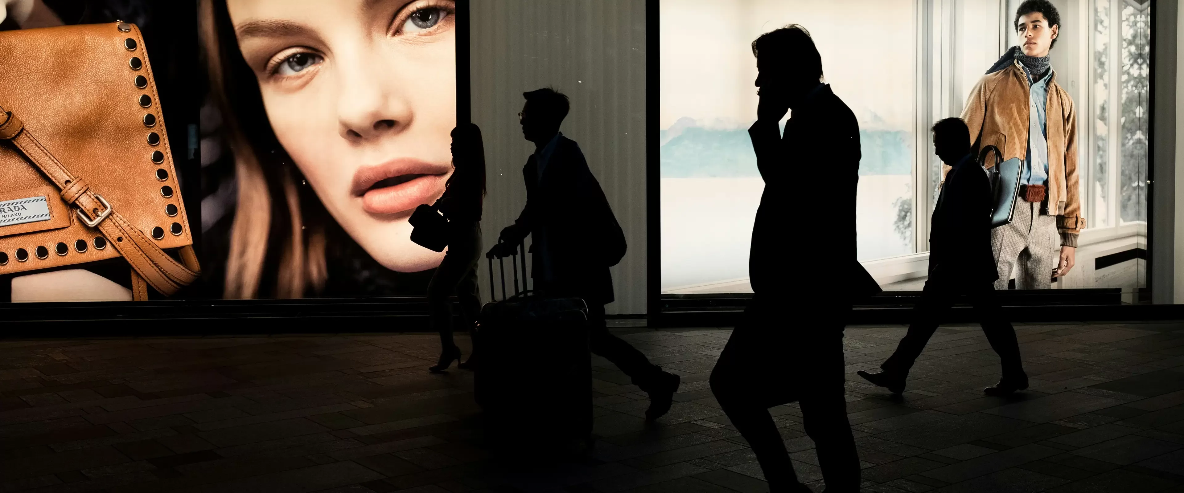 Black silhouettes of people walking in front of colourful adverts on a building