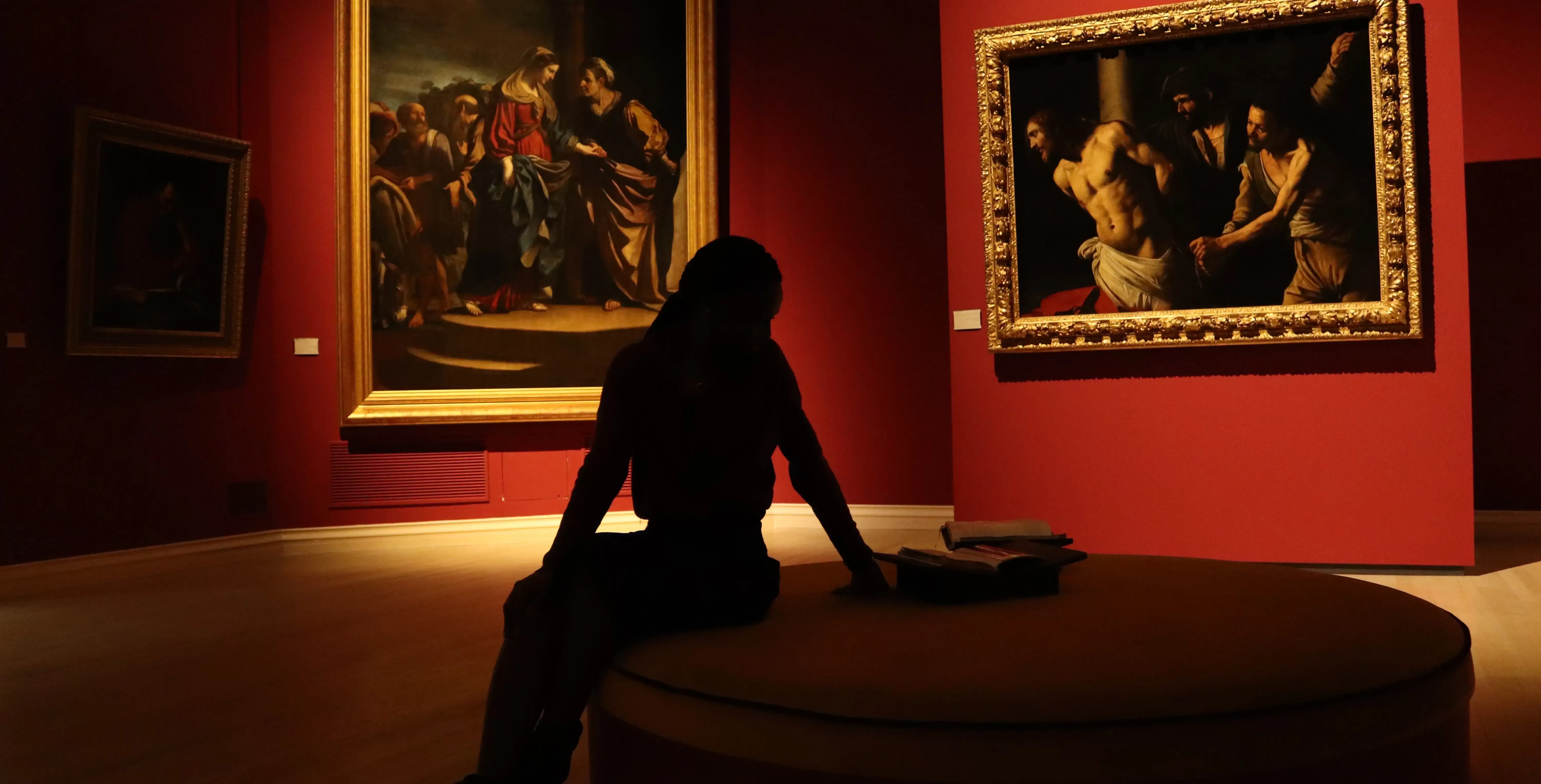 Women sat with arm on center sofa in red art gallery