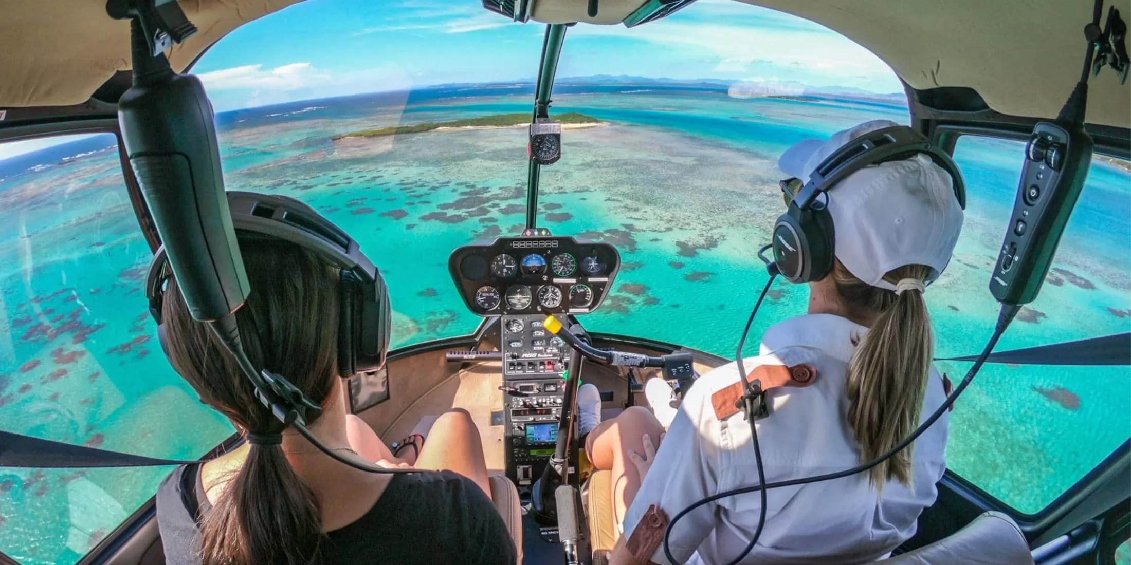Female passenger and female pilot in unfirm wearing flight gear, flying helicopter to private island hotel Miavana by Time + Tide, Madagascar.