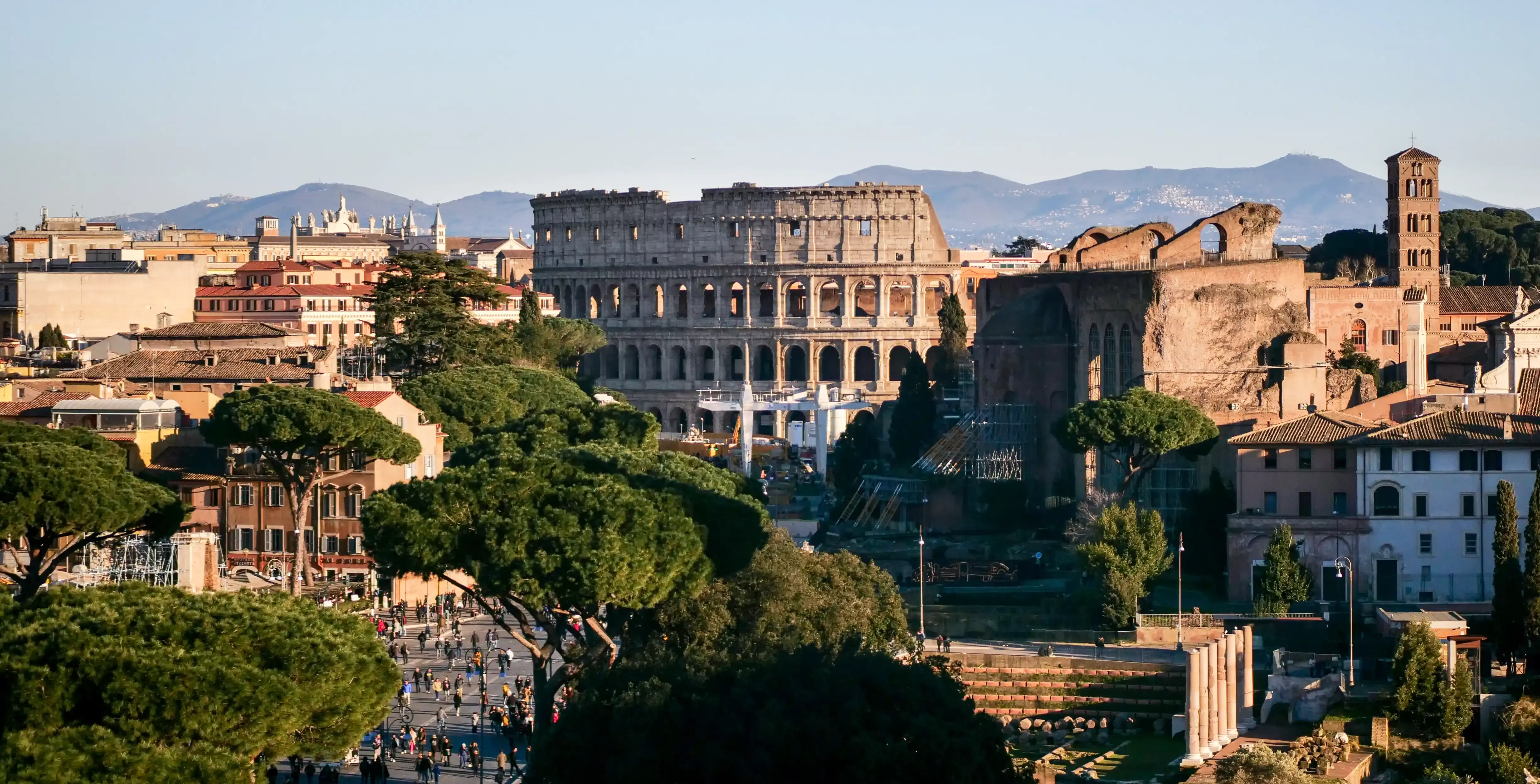 High up view of Rome city full of trees and buildings and the colosseum with hills behind it