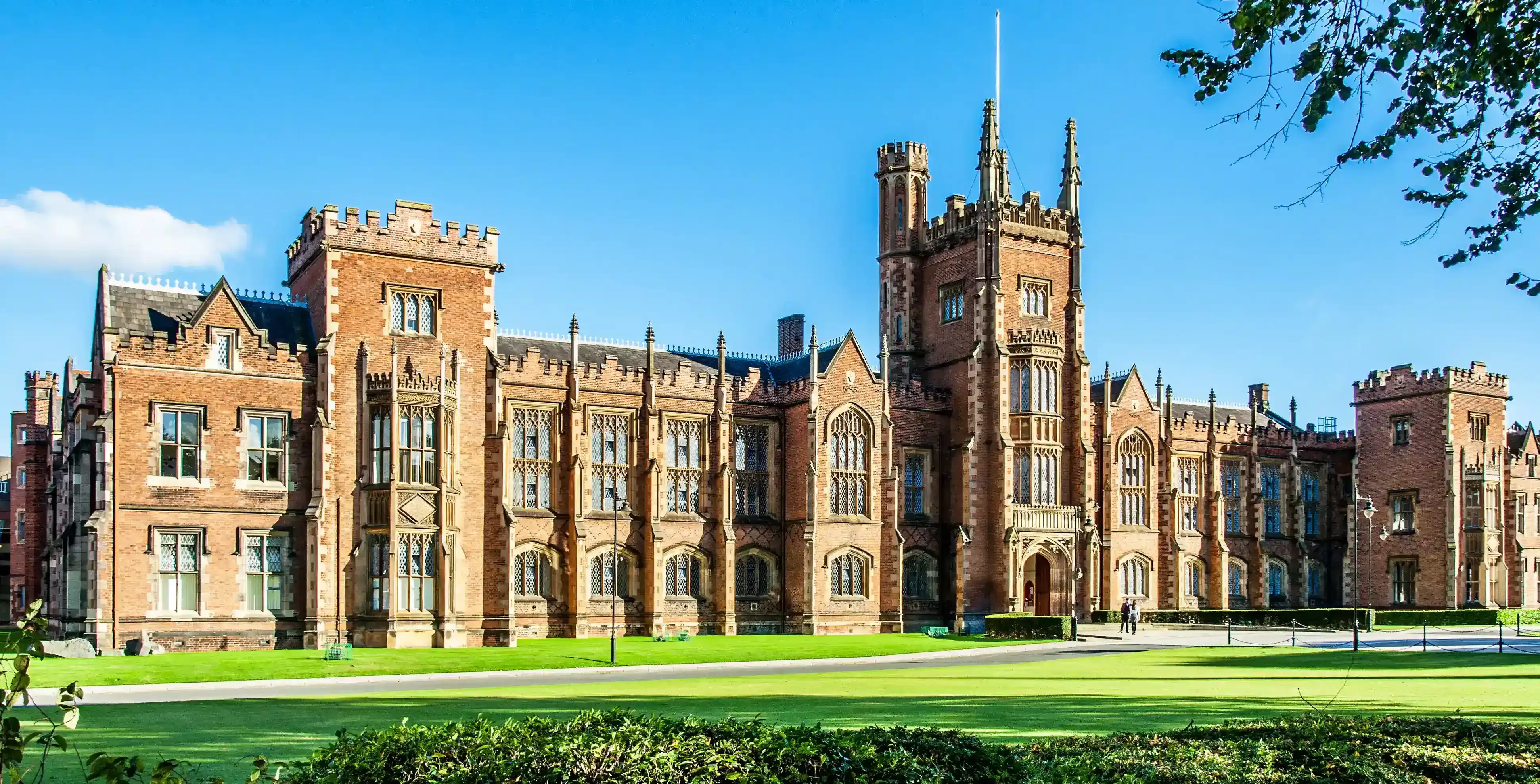 The Queen's University of Belfast with a grass lawn, tree branches and a hedge in sunset light
