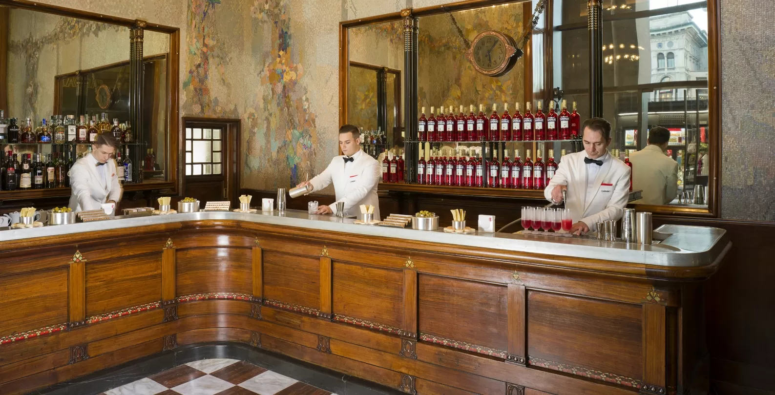Three men in suits making cocktails behind grand luxury bar