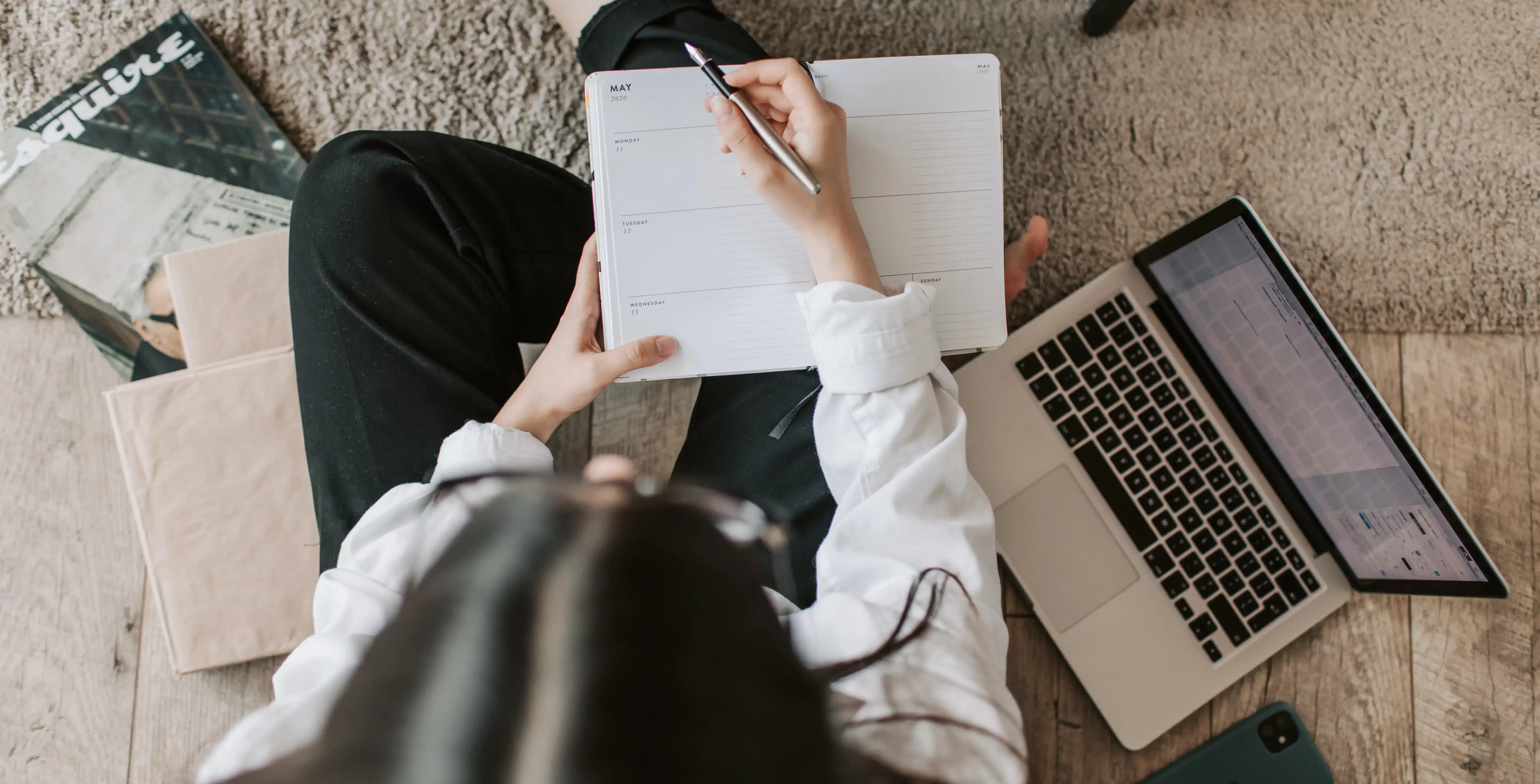 Women sat on carpet floor surrounded by laptop and notebooks writing in a diary