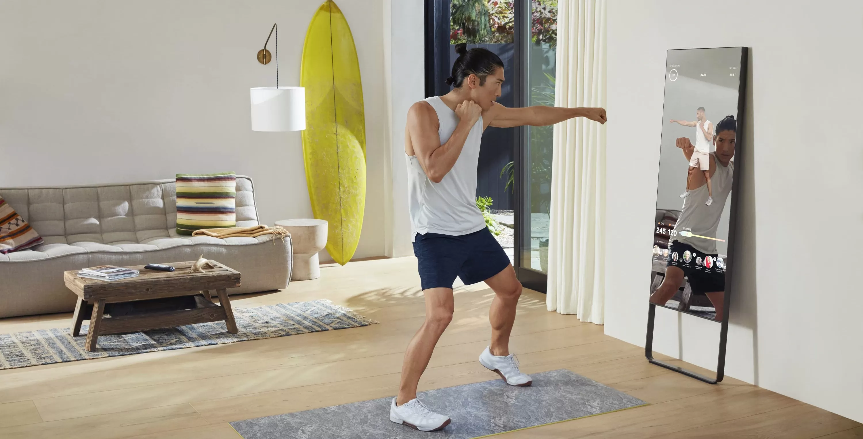 Man in gym clothes working out, doing punches opposite a home fitness technology mirror in a lounge room