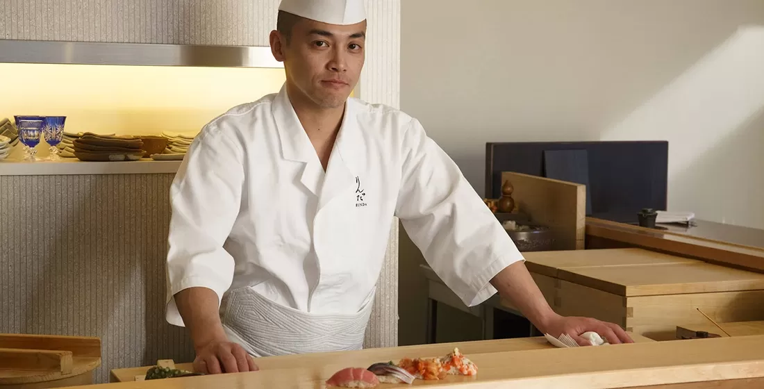 A chef in a white hat and shirt in a kitchen preparing sushi