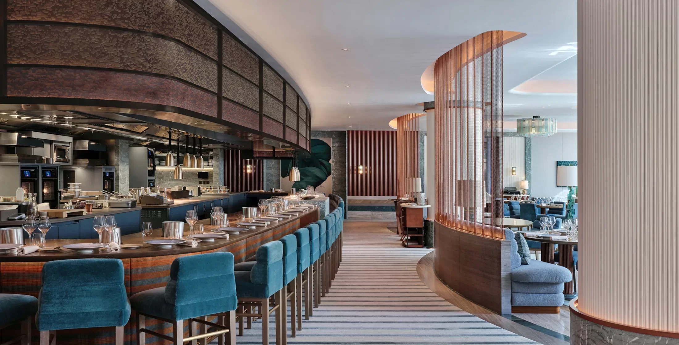 Luxurious modern restaurant interior with a curved bar lined with teal upholstered stools. The space features stylish partitions, ceiling lights, and dining tables set with glassware, creating an elegant and inviting atmosphere.