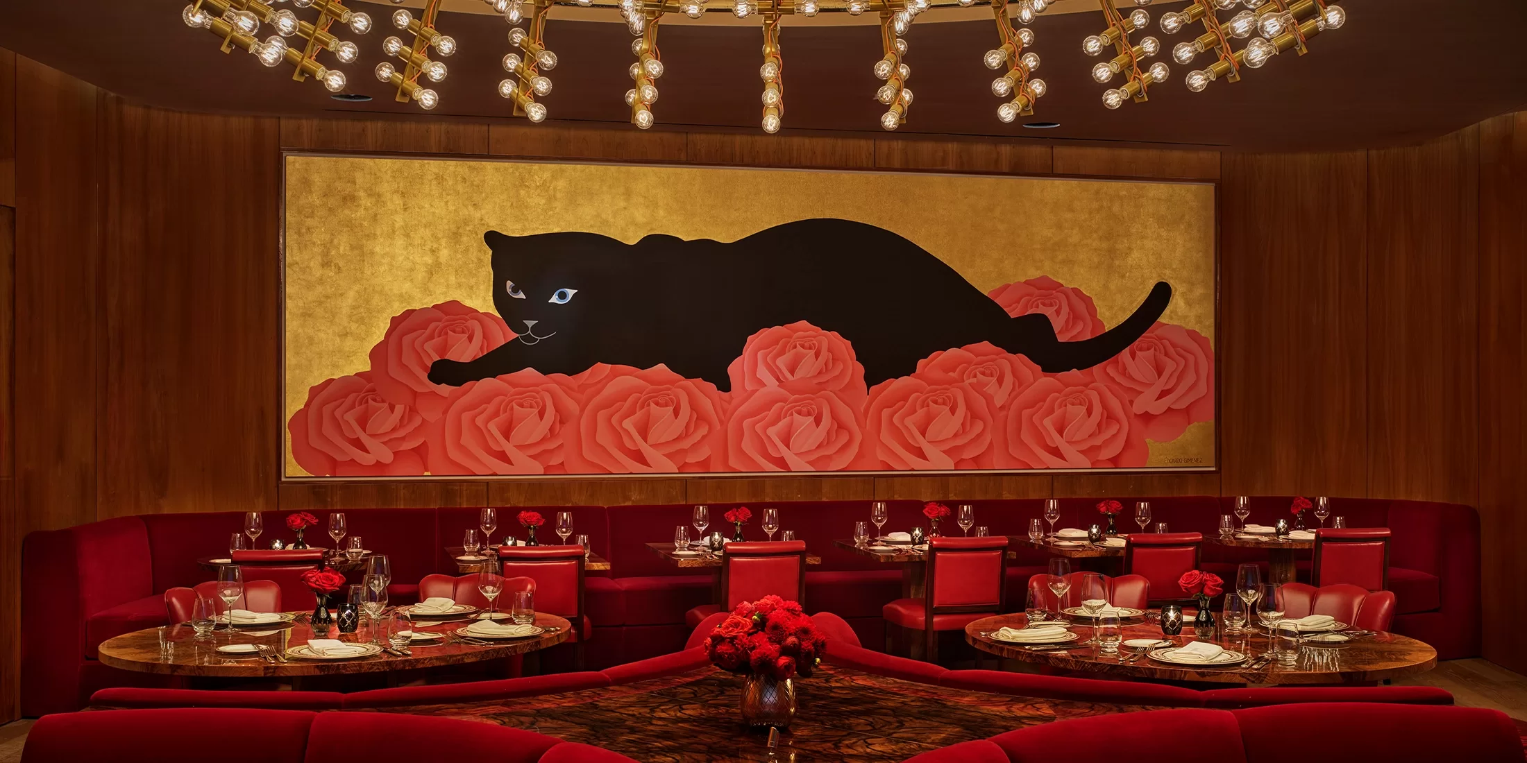 A luxurious restaurant interior with deep red velvet seating and elegant tables. A large painting of a black panther on red roses with a gold background hangs on the back wall under a modern chandelier.