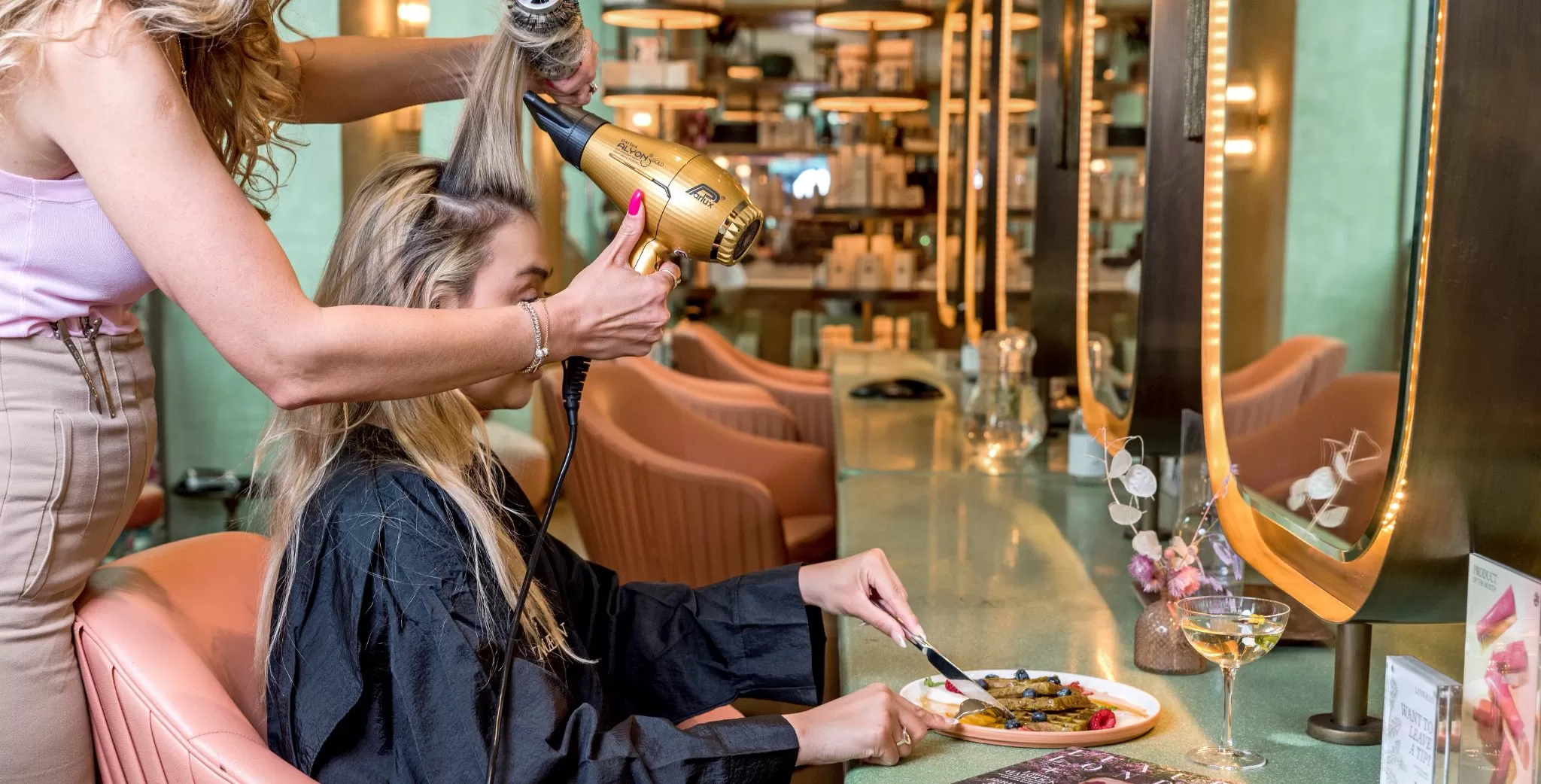 Women at Linnaen London hair salon getting hair styled by hairdresser whilst eating plate of food