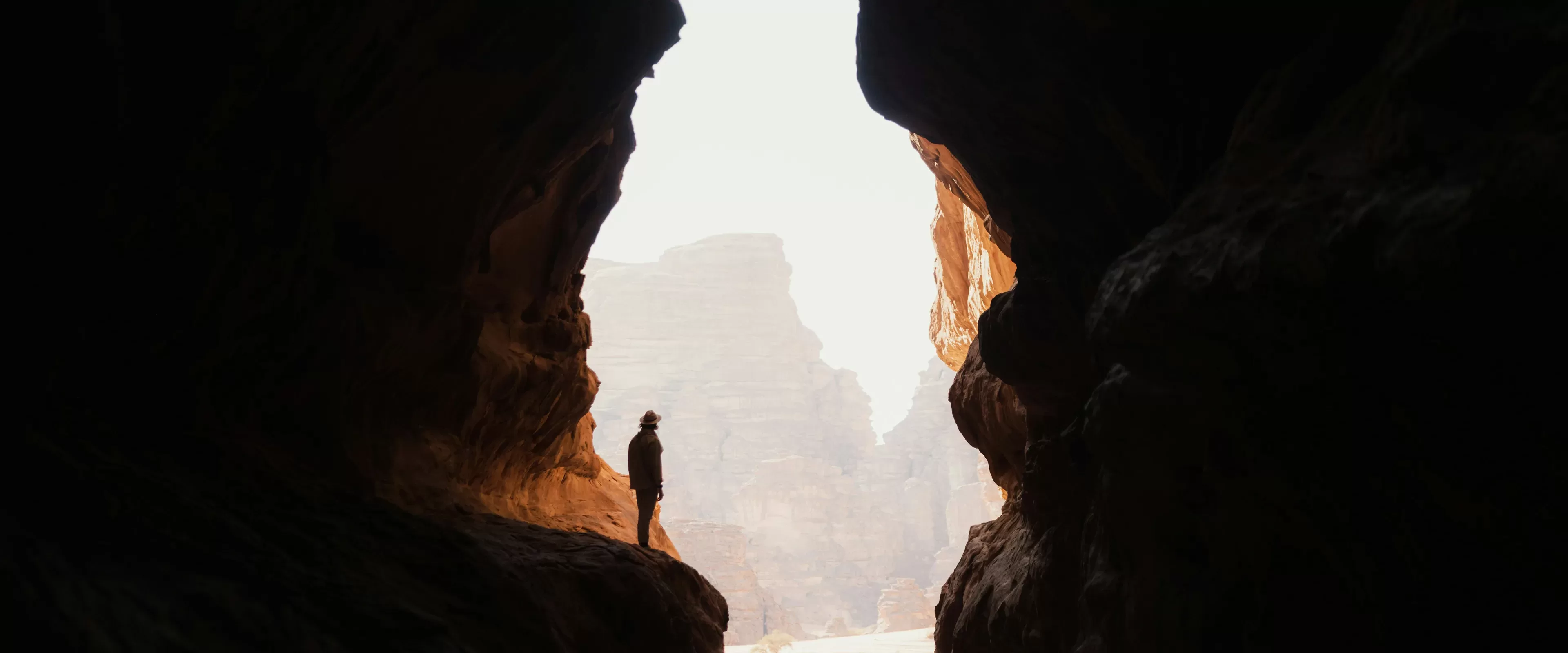 Photo of man standing on the ledge of a rock in between two giant mountainous rocks.