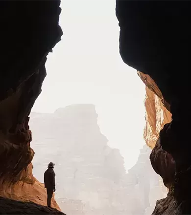 Photo of man standing on the ledge of a rock in between two giant mountainous rocks.