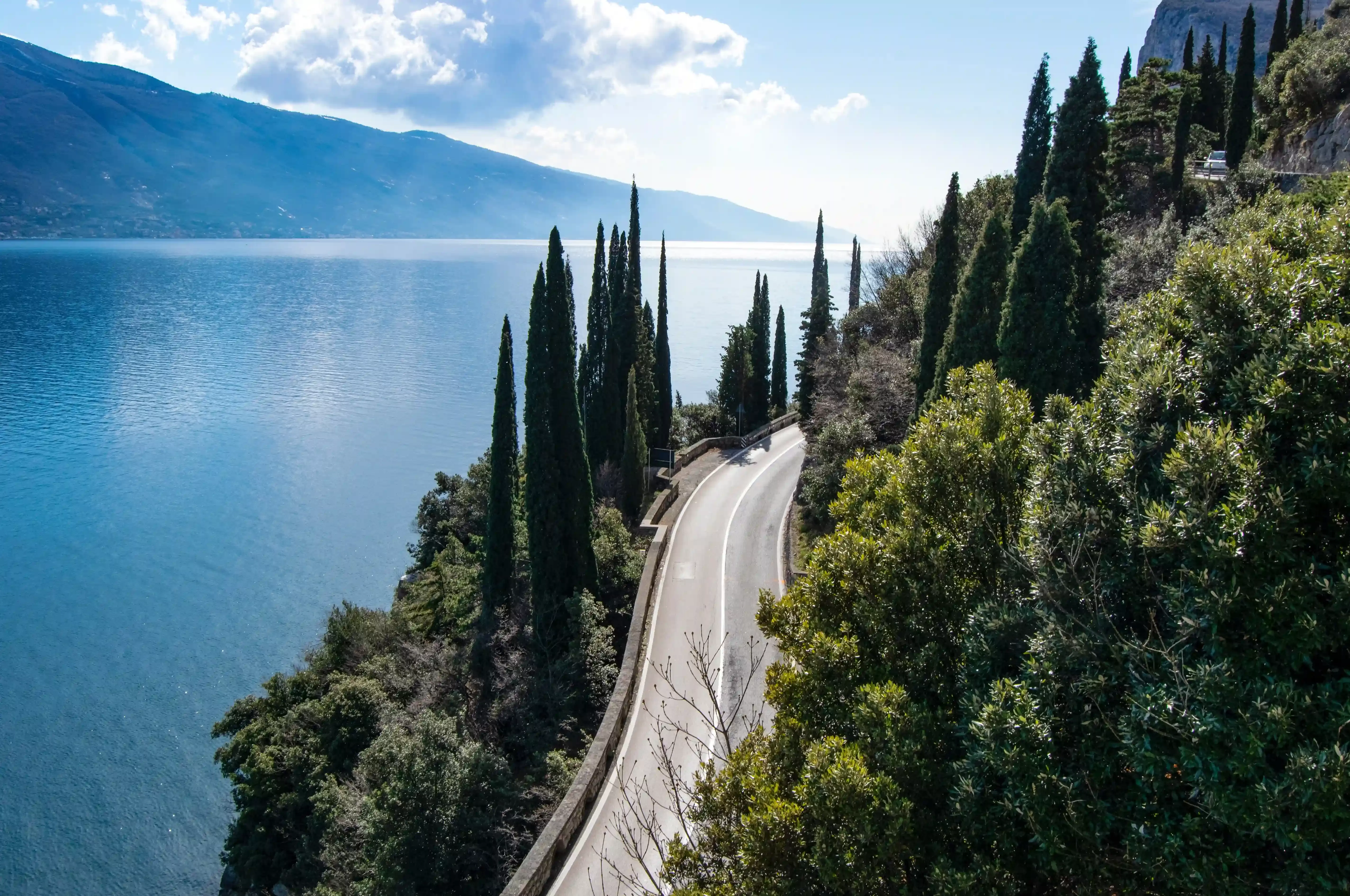 Road through a hill full of trees overlooking Lake Garda and mountain