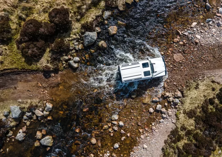 Birdeye eye view of the INEOS Grenadier by Sir Jim’s lieutenants off-road driving through water and rocks in the Cairngorms, Scotland.