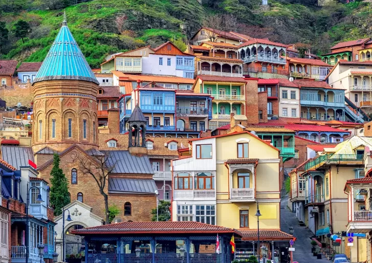 Beautiful landscape photograph of buildings on a hill side in different colours including blue, rusted red and yellow in Tbilisi