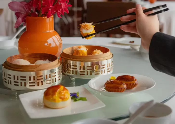 Person with chopsticks, eatting from a variety of dim sum in plates and bamboo bowls at Lung King Heen, Hong Kong.