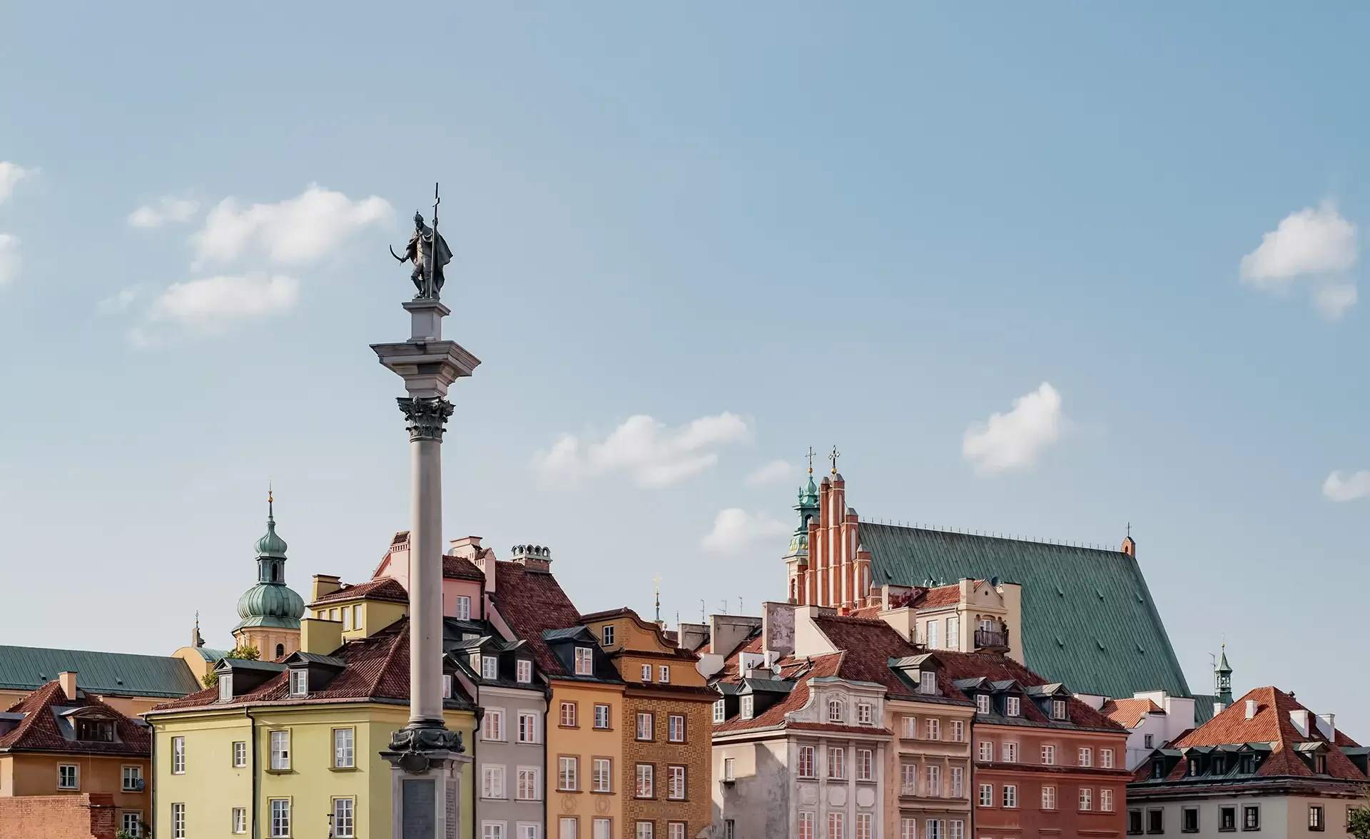 Colorful historic buildings line a street beneath a clear blue sky in Warsaws Old Town. A tall column topped with a statue stands prominently in the foreground.